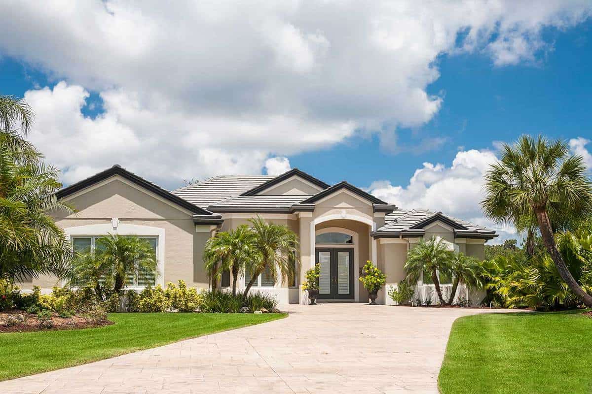 New luxury home in the tropics with driveway, palm trees, lush tropical foliage on front lawn
