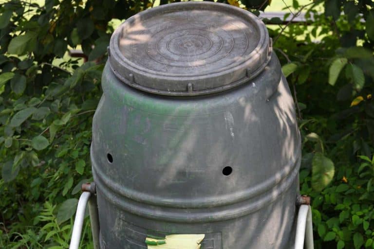 Closed compost tumbler outside yard full of grass