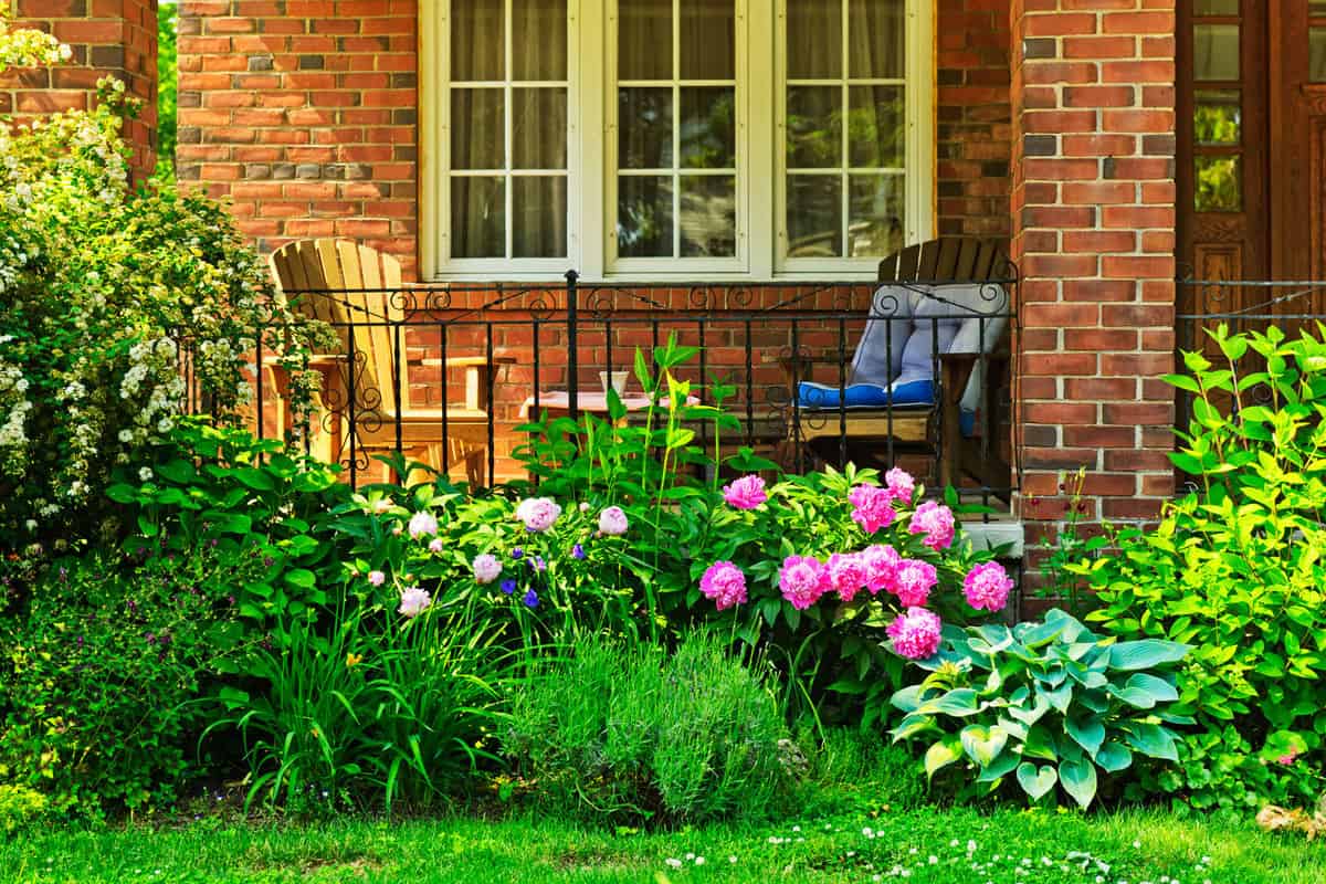 A brick front porch with a garden with lots of flowers