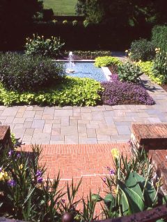 A spacious and modern garden with brick and stone flooring with a center aisle filled with flowers, 5 Of The Best Plant-Safe Concrete Cleaners
