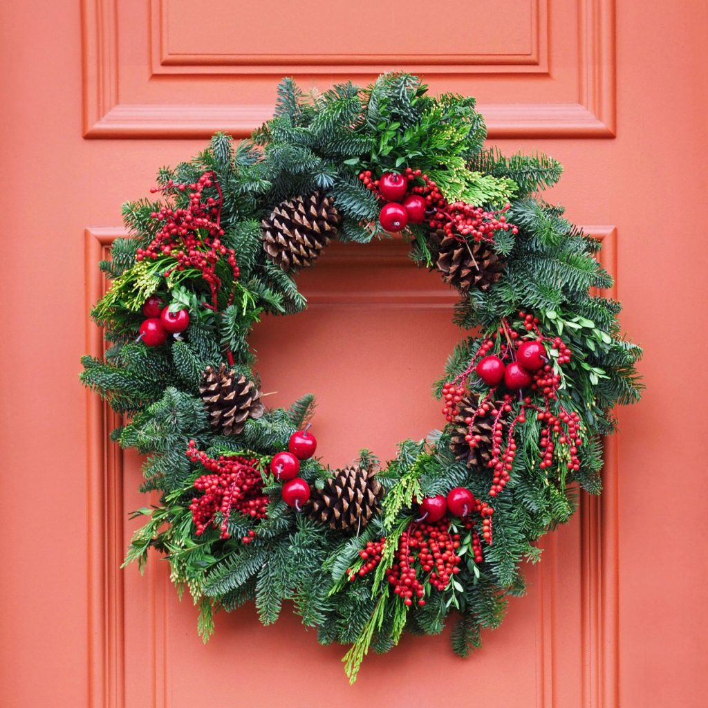 A wreath decorated with pine cones, holly hock berries and pine leaves to a front door
