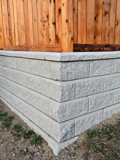 A beautiful close-up view of a residential garden block retaining wall with a new wooden fence build behind. Should You Add A Fence To A Retaining Wall [And How To Do So]