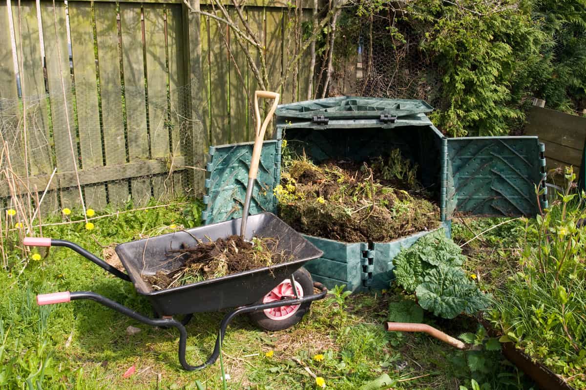 A compost bin with a wheel barrow on the side with a shovel, How To Store Compost In The Winter [9 Solutions To Consider]