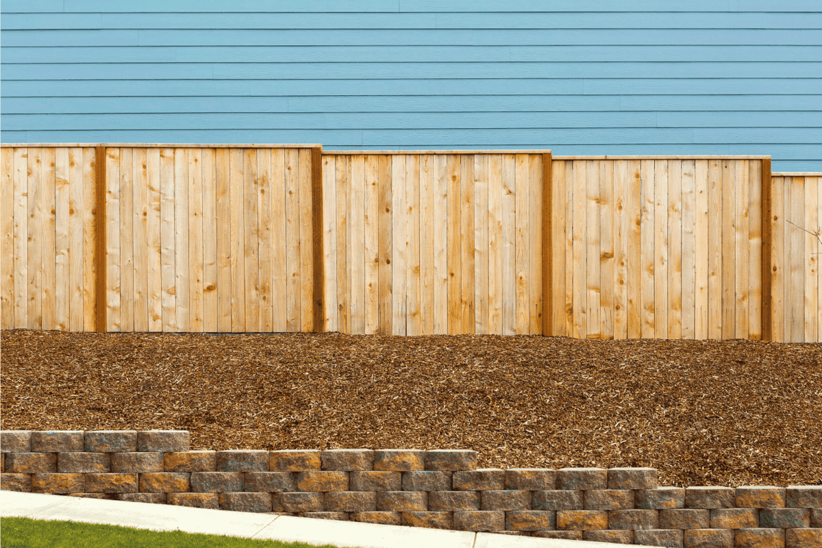 New Garden Wood Fence with house siding and barkdust mulch with concrete retaining wall along exterior sidewalk
