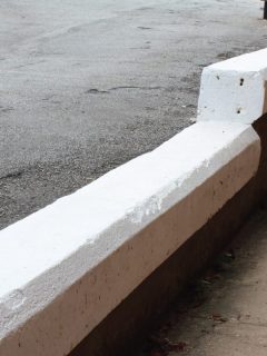 Painted thick white concrete curb between elevated road and sidewalk. Can You Build A Retaining Wall On Concrete [Plus How-To Tips]