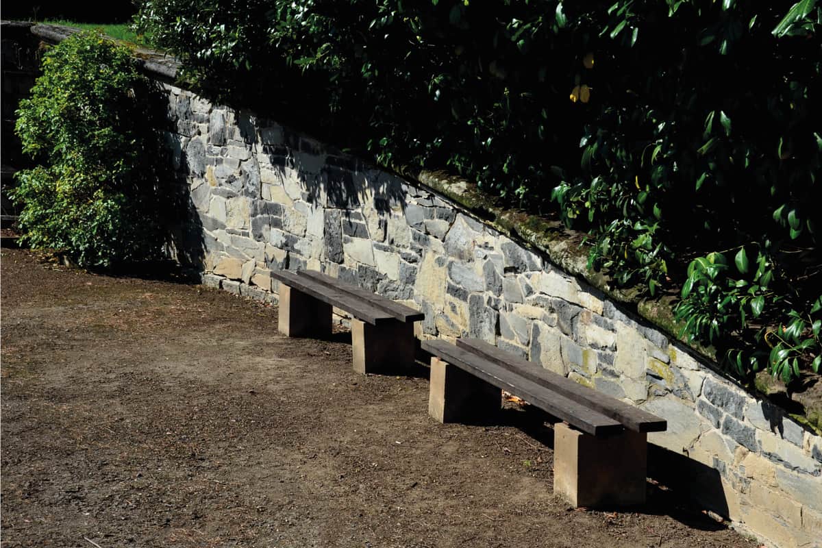 benches under the retaining wall in an Italian baroque garden. the wall slopes to the side and is finished with a stone carved volute in the shape of a spiral.