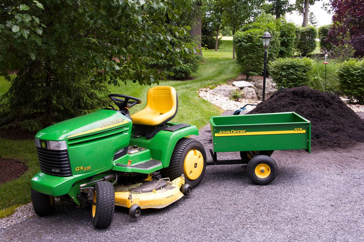 A green John Deere lawn mower with a collector towed on the back