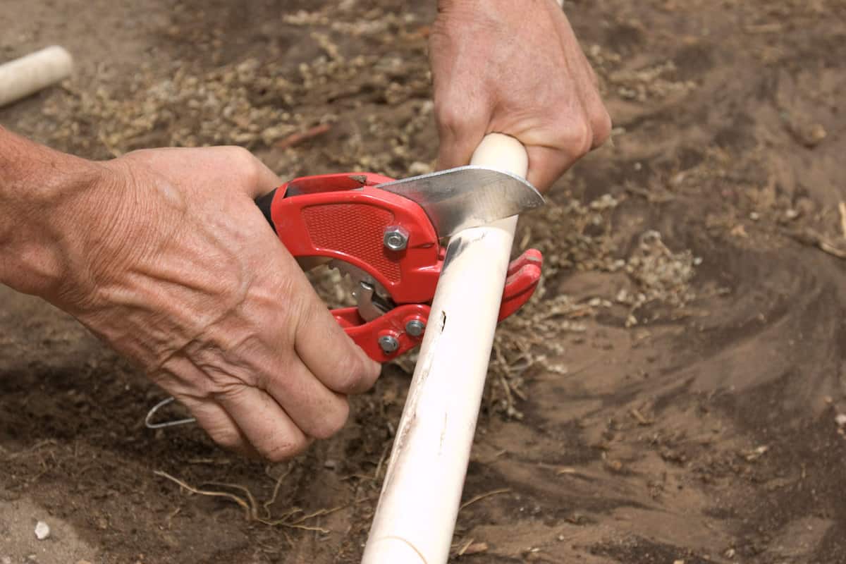 A landscaper cutting a white PVC pipe