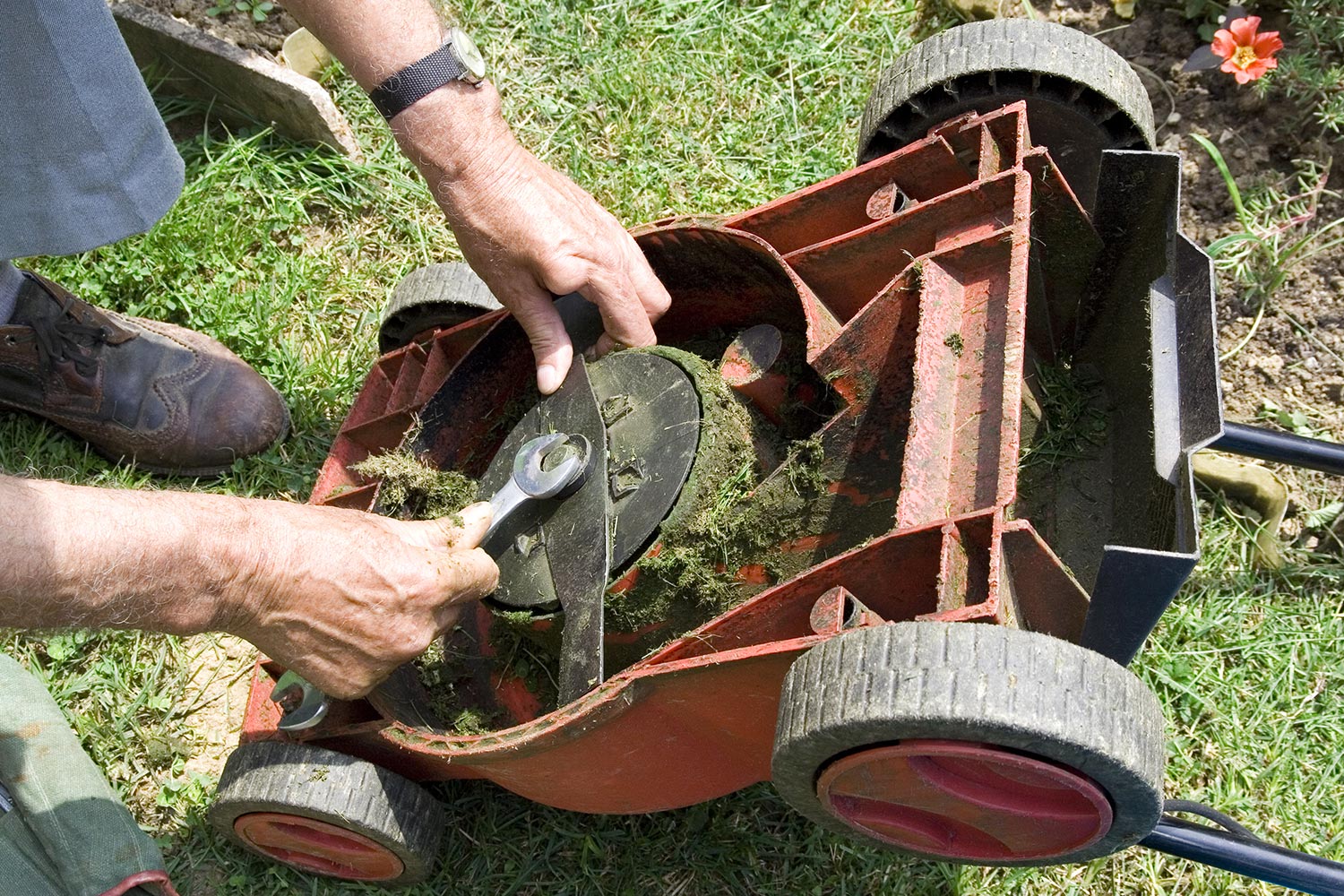 Hands fixing an overturned lawnmower with wrench