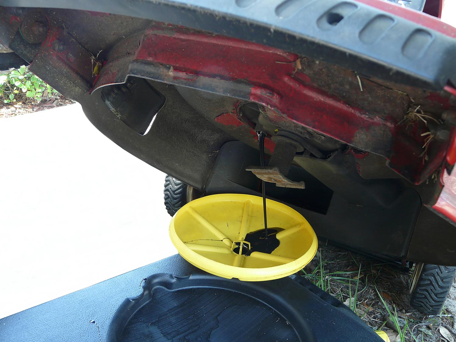 Oil draining into a yellow and black container during an oil change on a red lawn mower