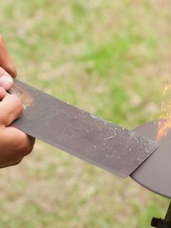 Sharpening Lawn mower blade by holding it by two hands in outdoor, What's The Best File For Sharpening Lawn Mower Blades?