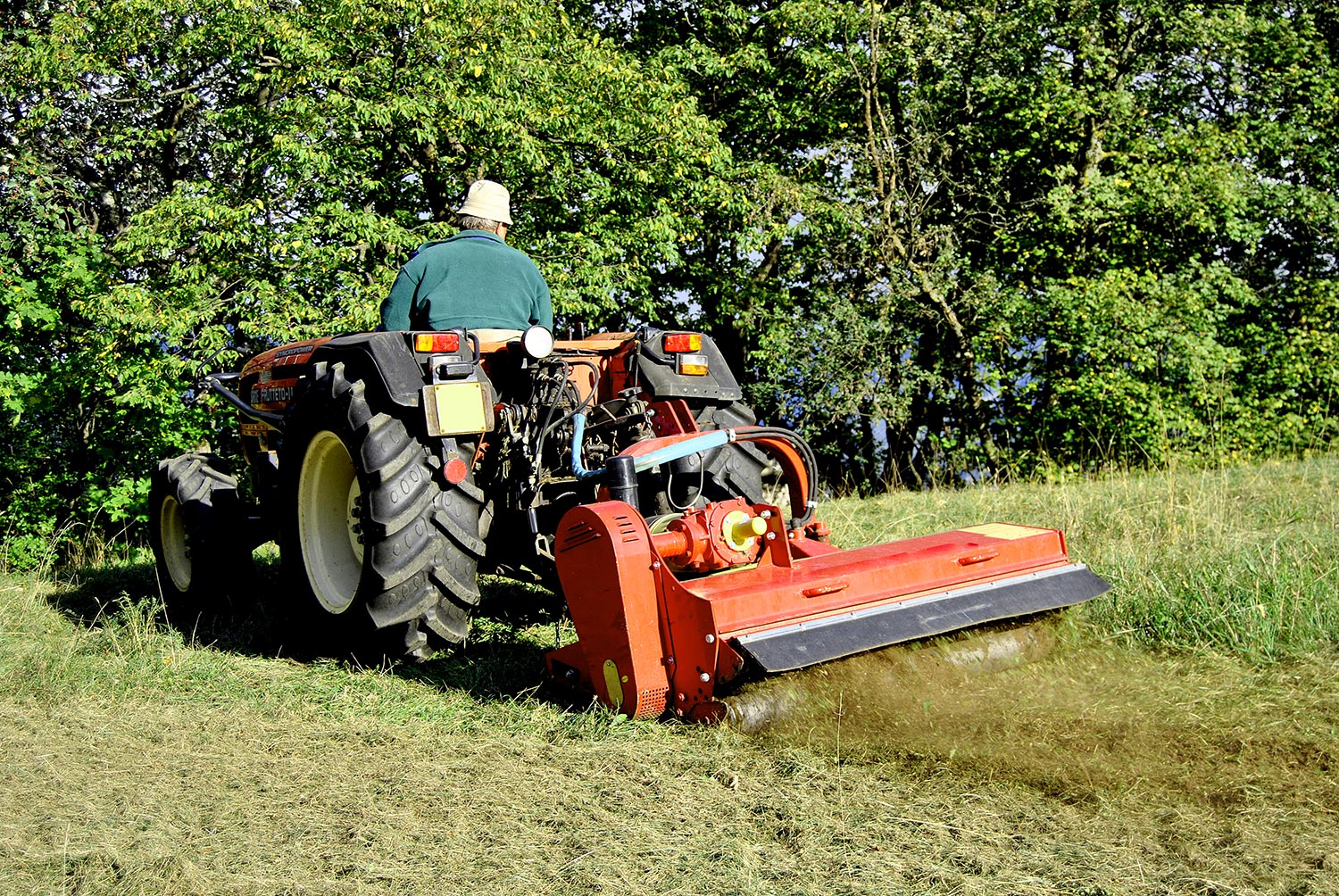 Small farm tractor bush hogging on a grass field