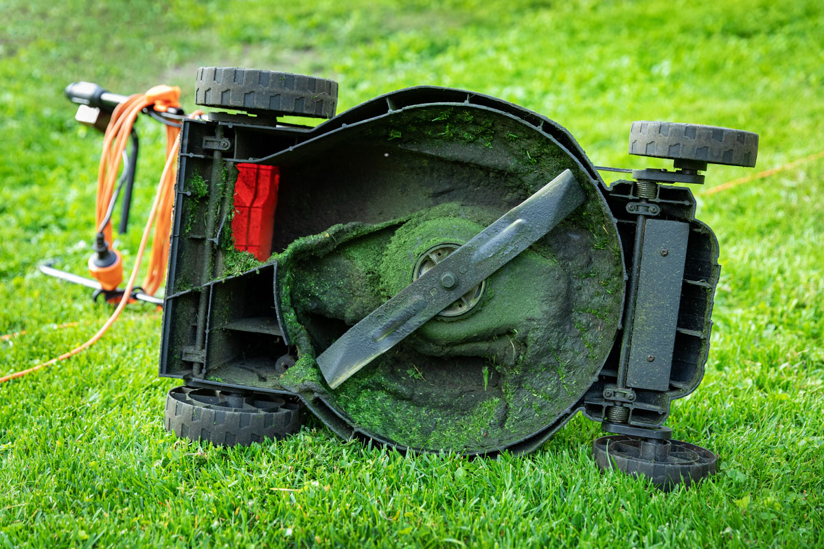 dirty electric lawn mower flipped in green grass at home