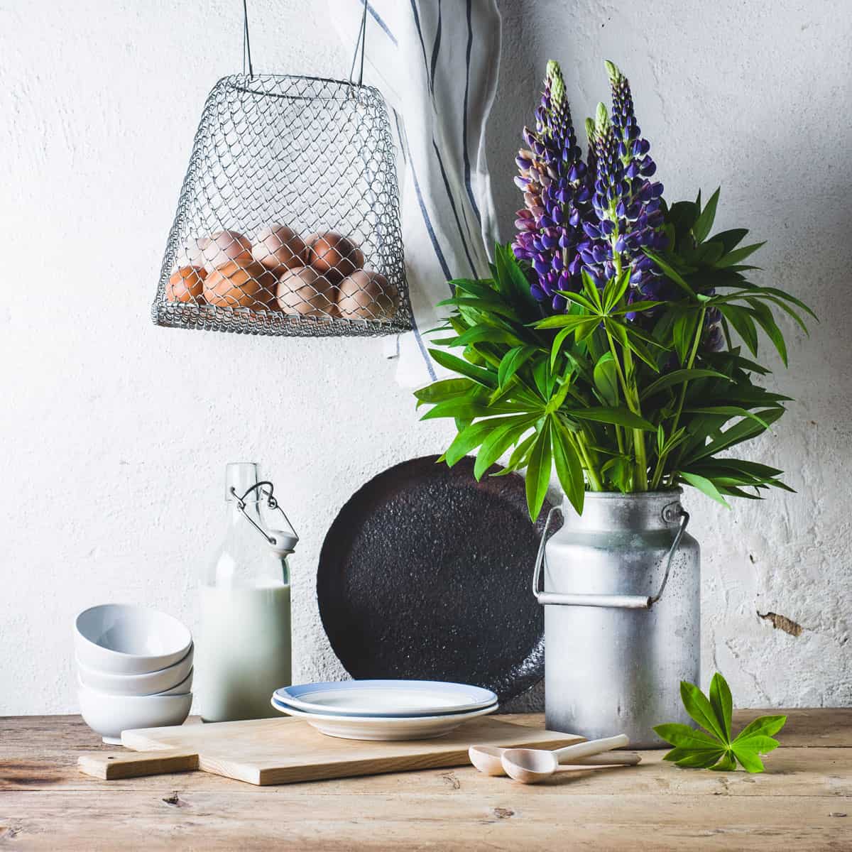 A kitchen counter with kitchen utensils and a small stainless pot with lupin flowers