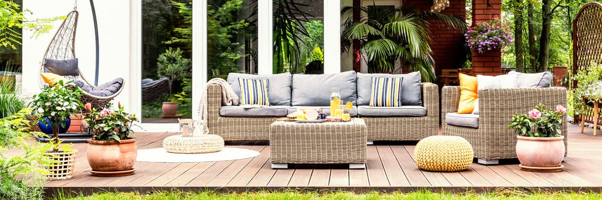A relaxing spot for a warm, summer day - a stylish, wooden terrace with wicker garden furniture, cushions, plants and flowers