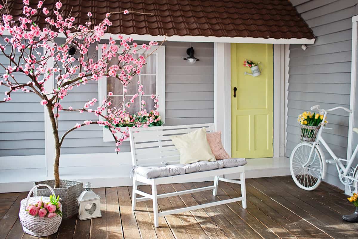 Bench standing near a white wooden house, cherry blossoms, a bicycle with tulips in a basket