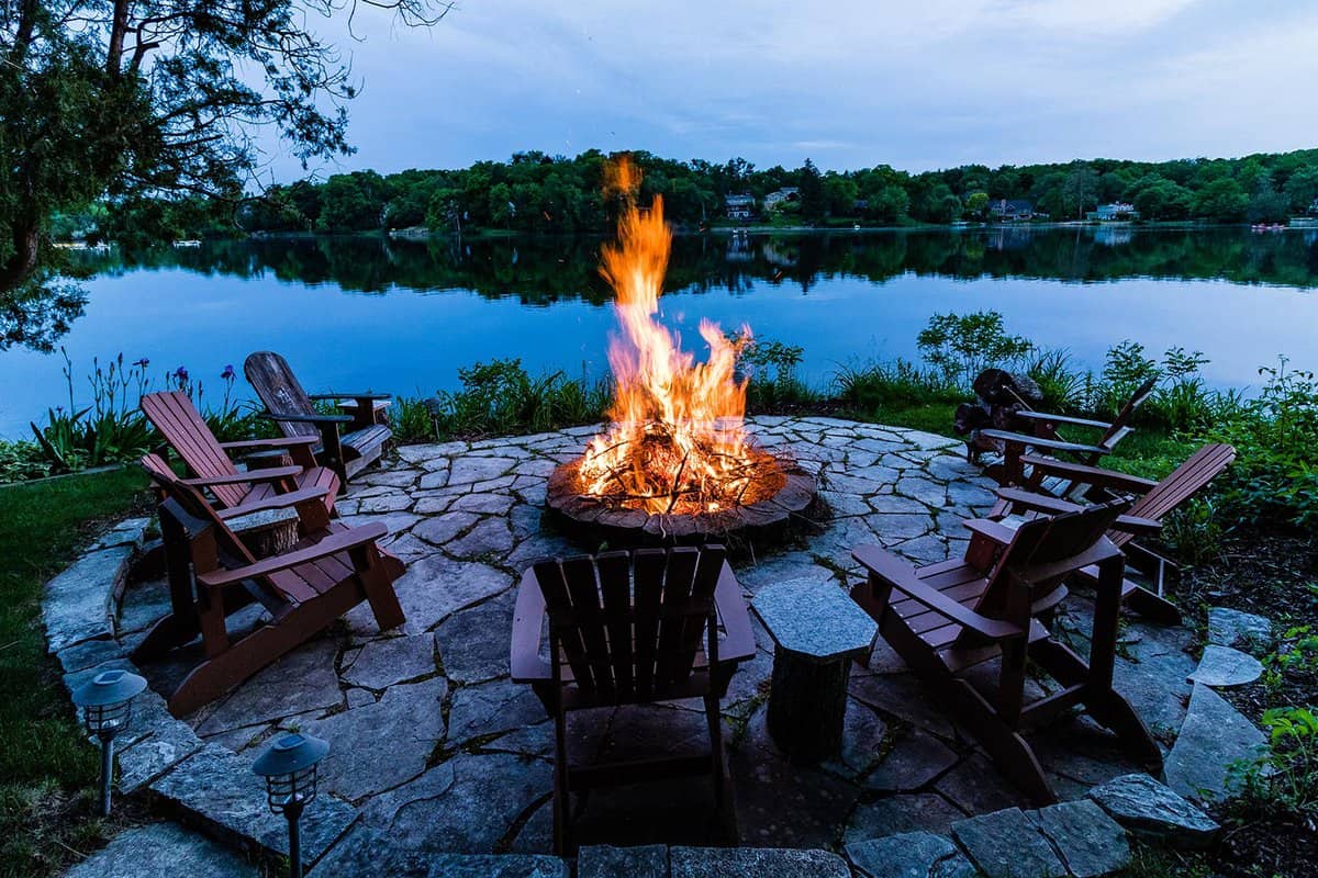 Deck chairs around a fire pit on the edge of a lake at dusk