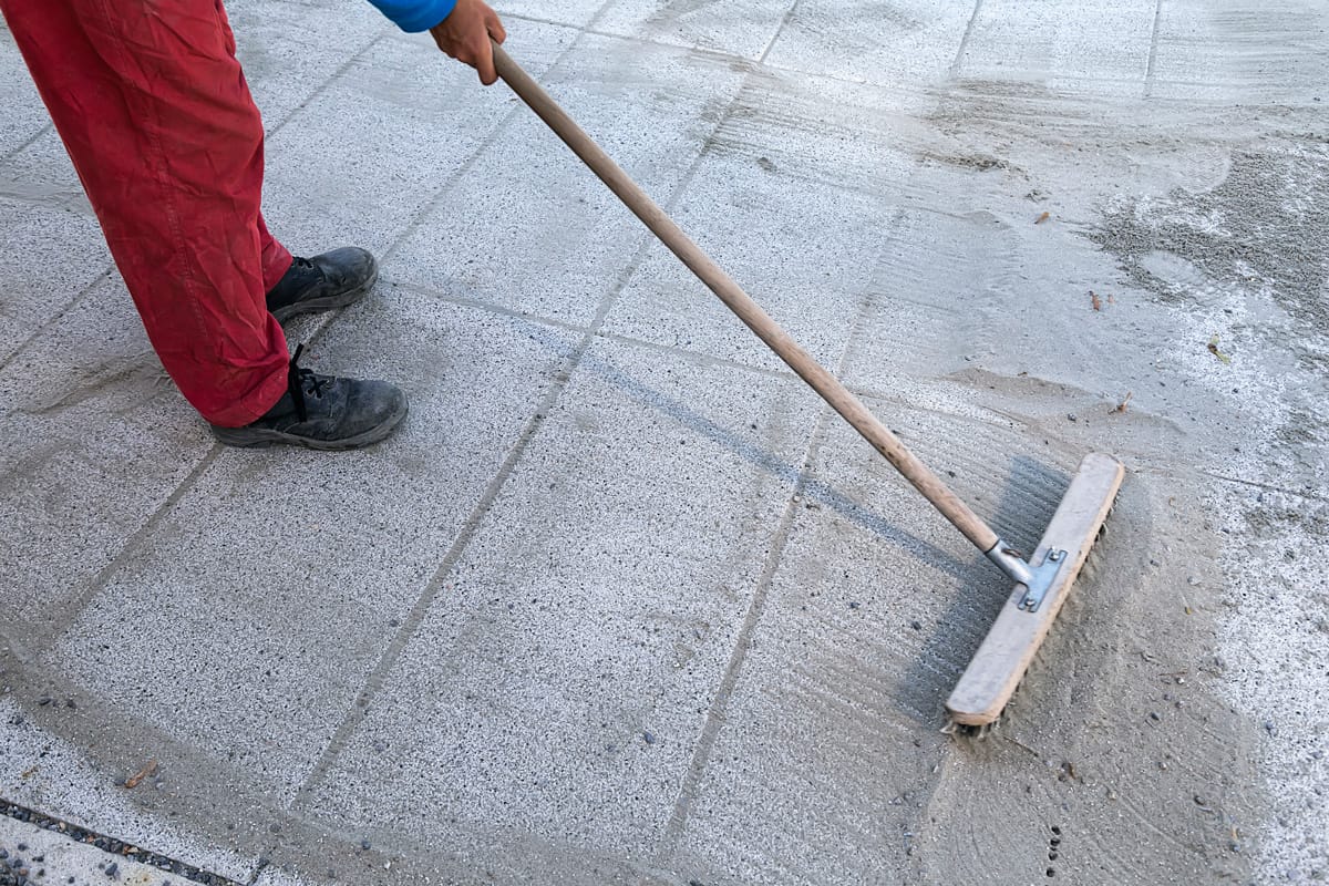 Install polymeric sand by brooming it into the paver joints during construction works. Some motion blur present.