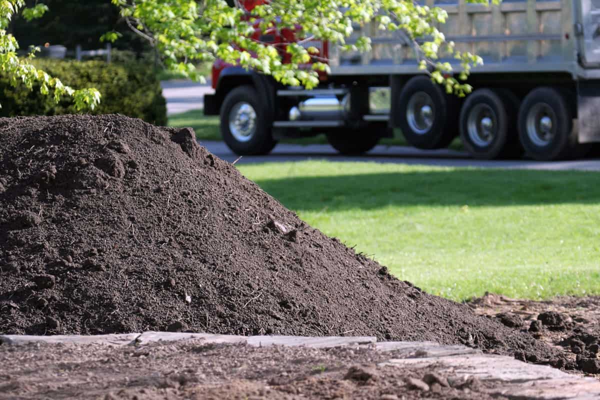 Large Dump Truck leaves residential property after delivering pile of topsoil