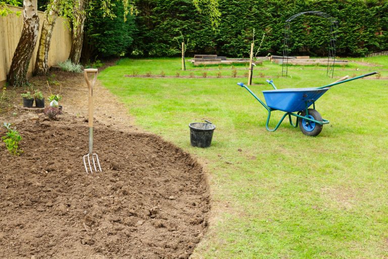 Preparing a freshly dug flower bed for planting in a garden with fork and wheelbarrow, Can I Put Topsoil Over Existing Grass And Reseed?