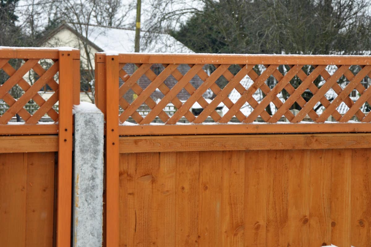 Wooden panel boundary fence with lattice trellis on top. Cold snowy winters day