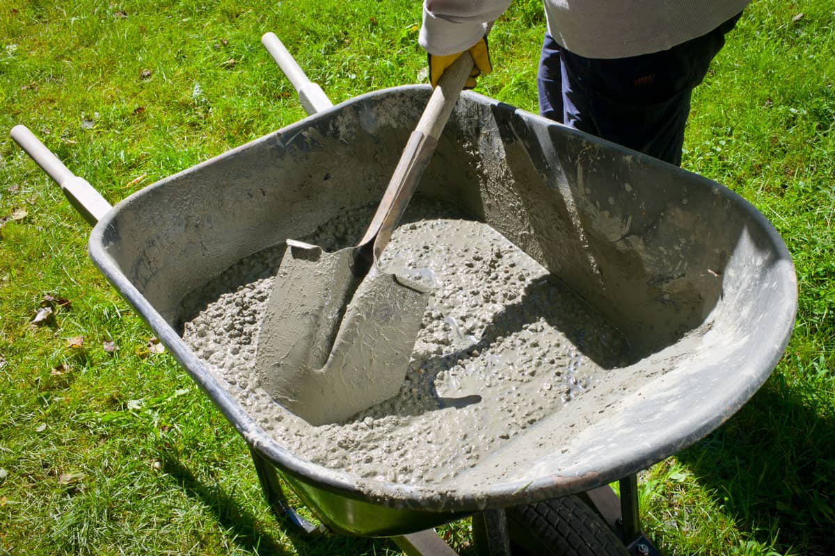Worker mixing concrete on the wheel barrow to build a fence
