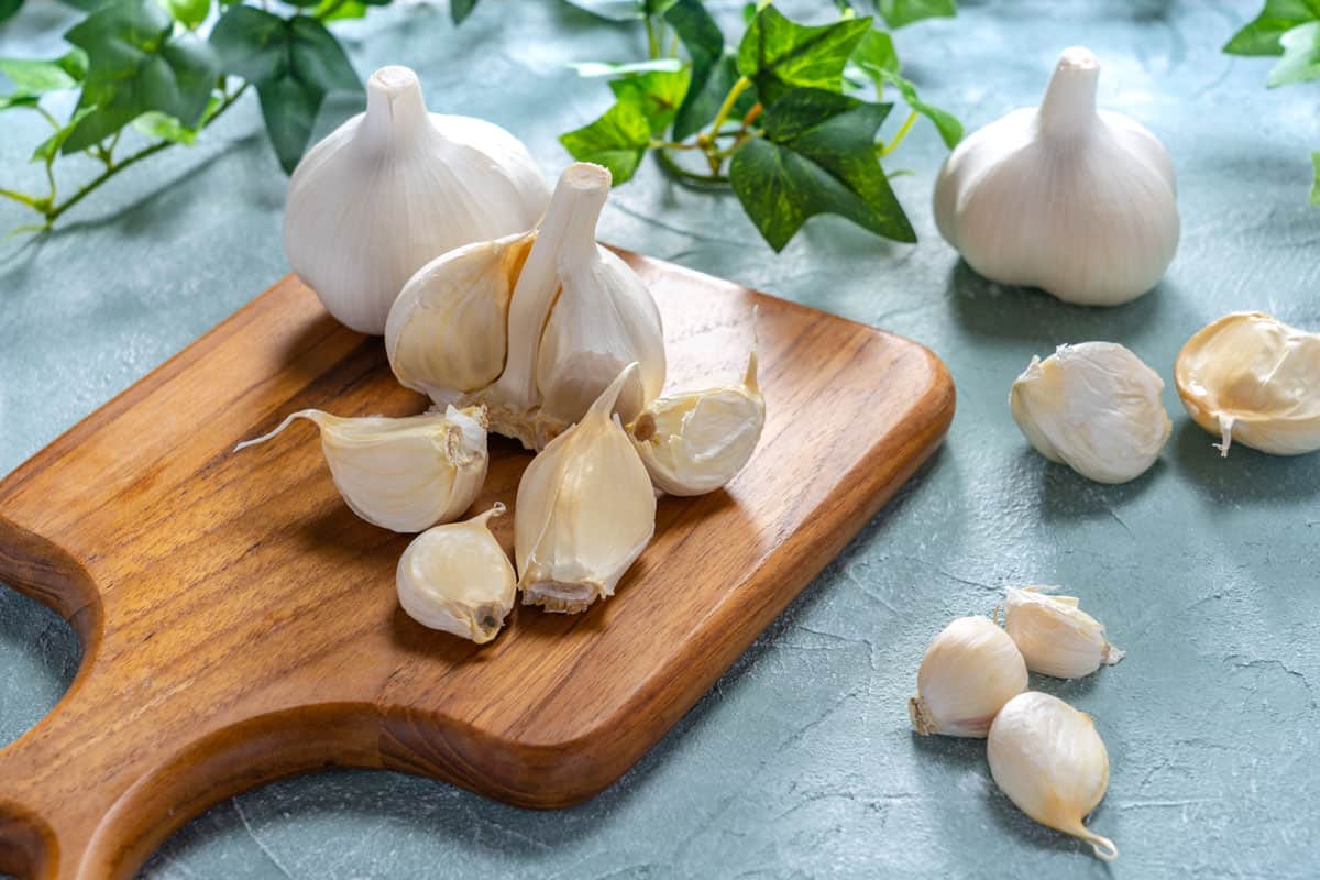 freshly bought garlic bulbs on top of a wood chopping board