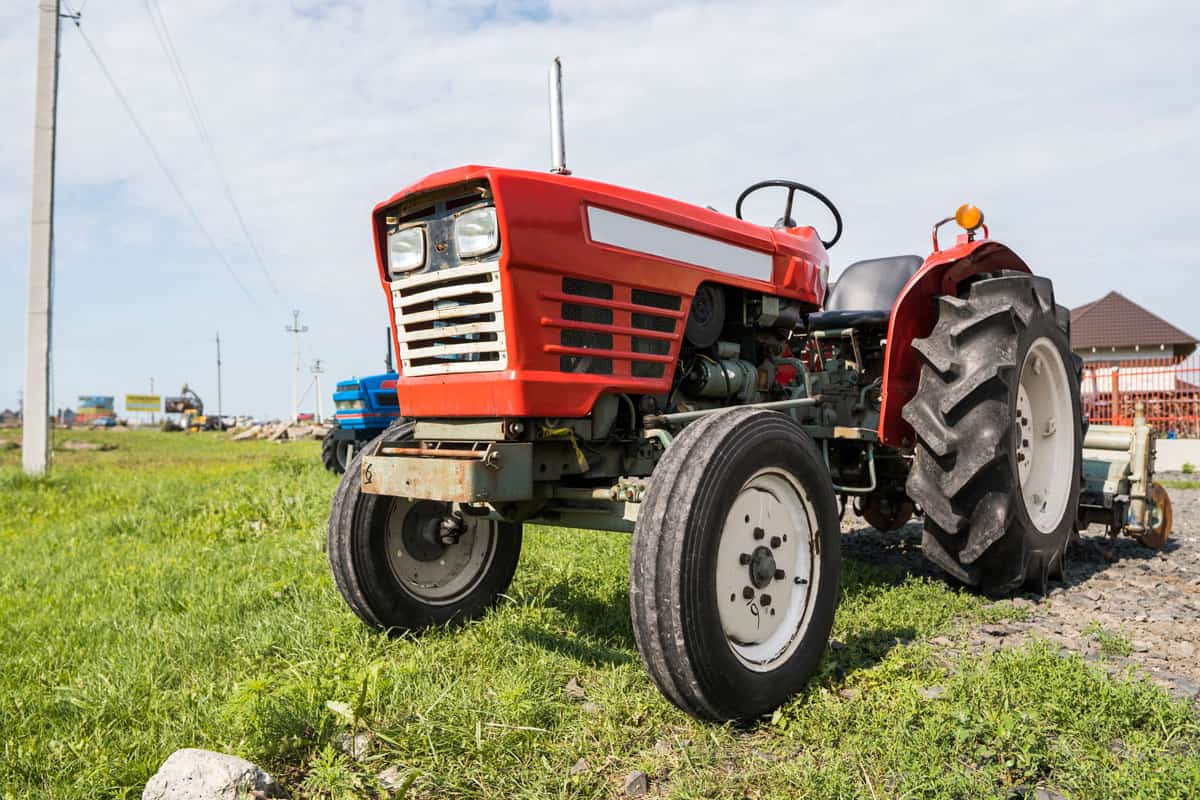 A small mini red tractor stands on a farm yard on green grass and waits for work to begin