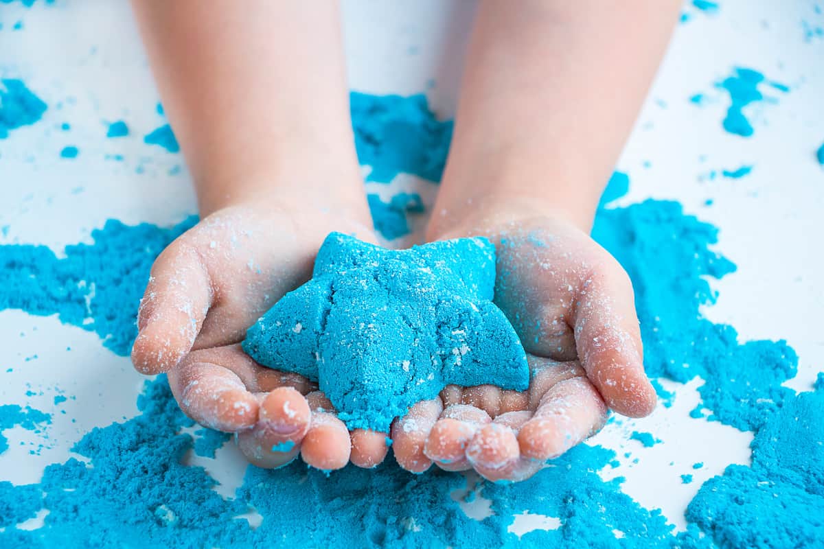 Baby hand making a blue star made from play sand