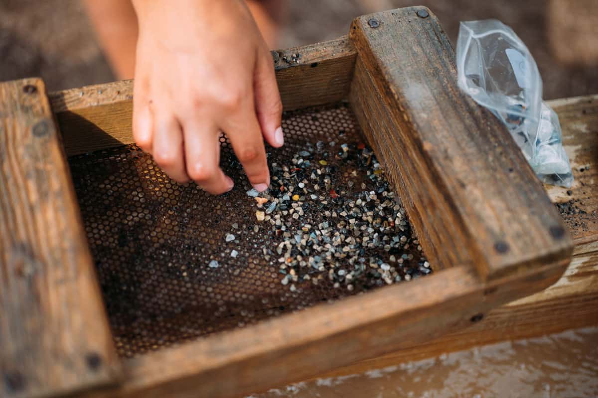 Children's hands using a sifter to sift sand and dirt to reveal crystals and gemstones