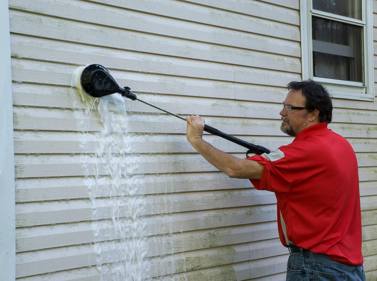 Using a high pressure brush to clean algae and mold off vinyl siding