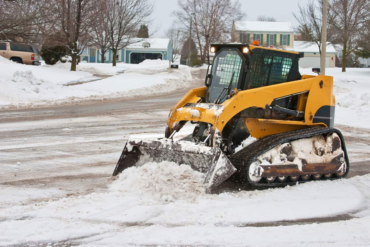 a small tracked type vehicle with a front end loader cleans up the snow
