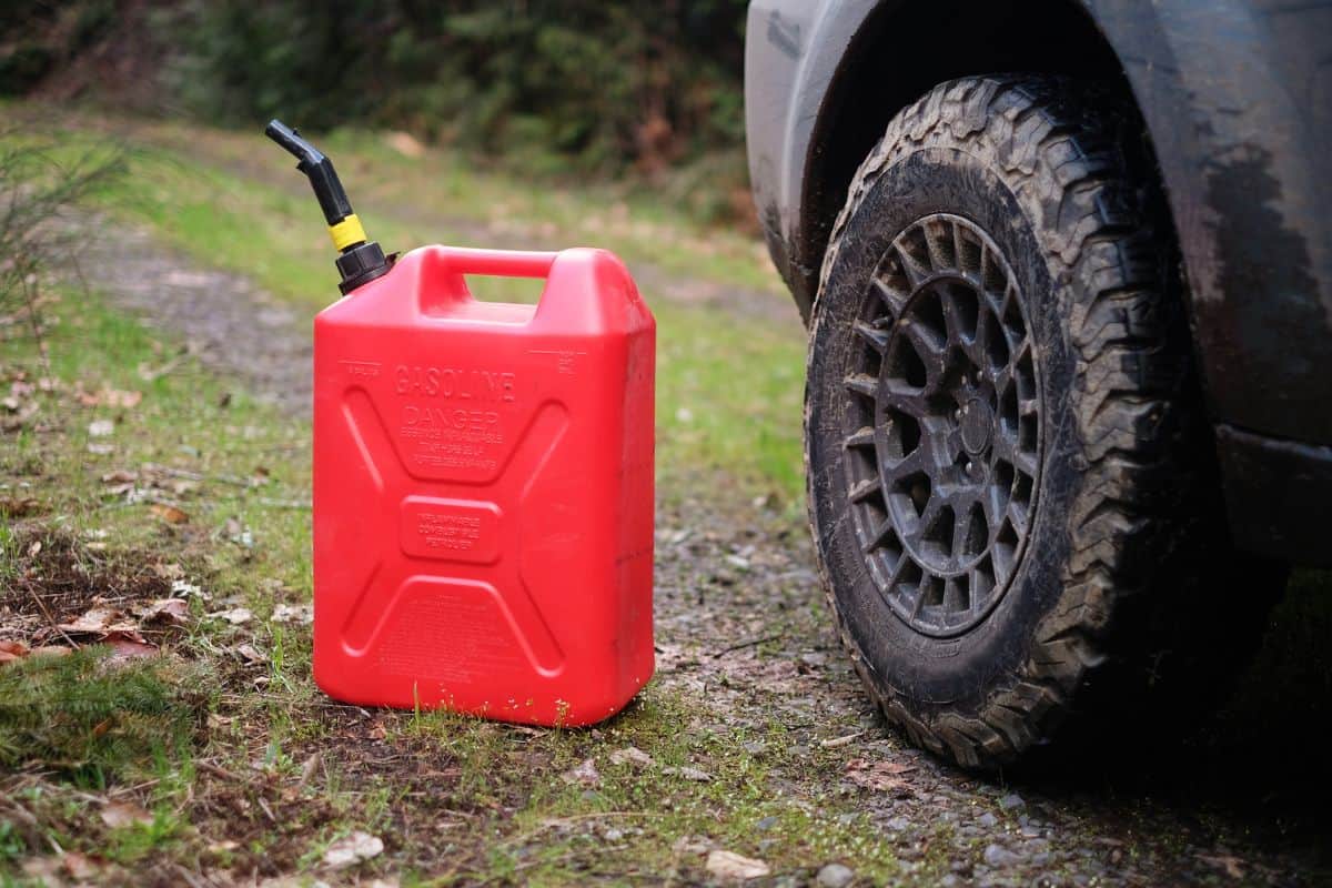 A 5-gallon gas can in use along a forest road next to unidentifiable vehicle