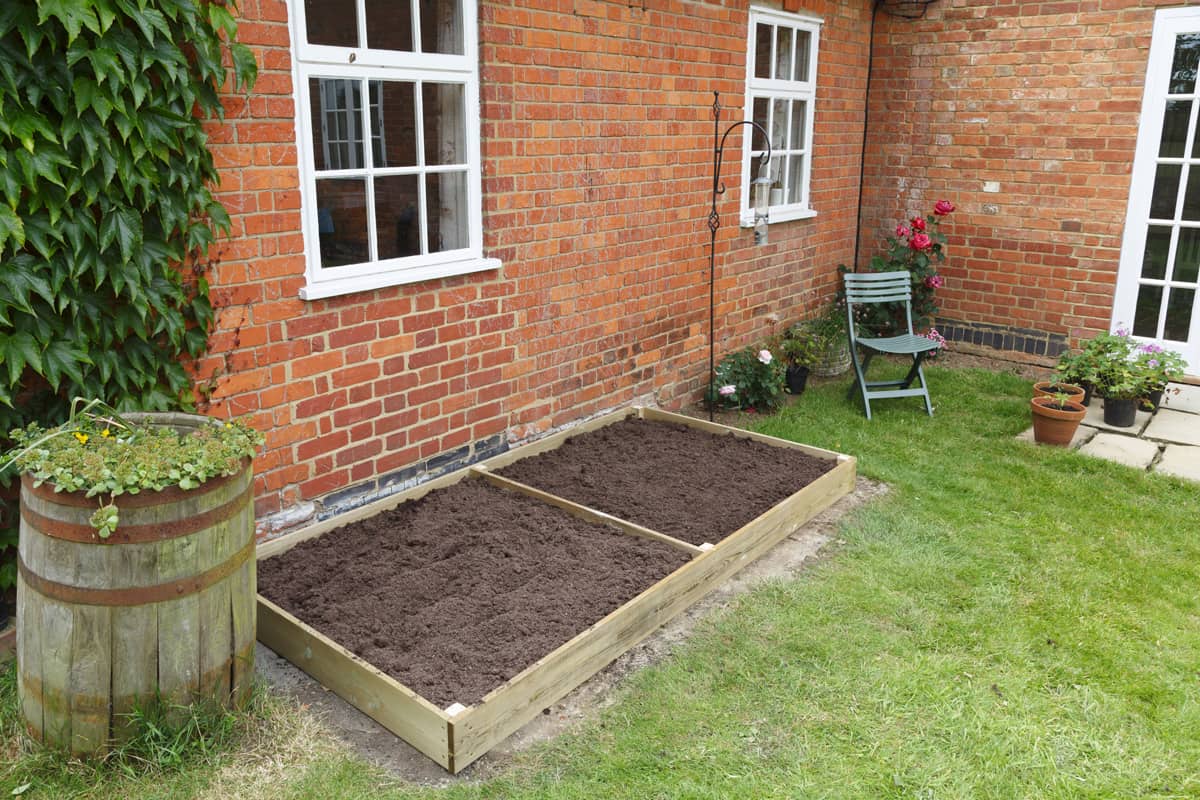 A new empty raised bed in a kitchen garden is filled with soil ready to plant