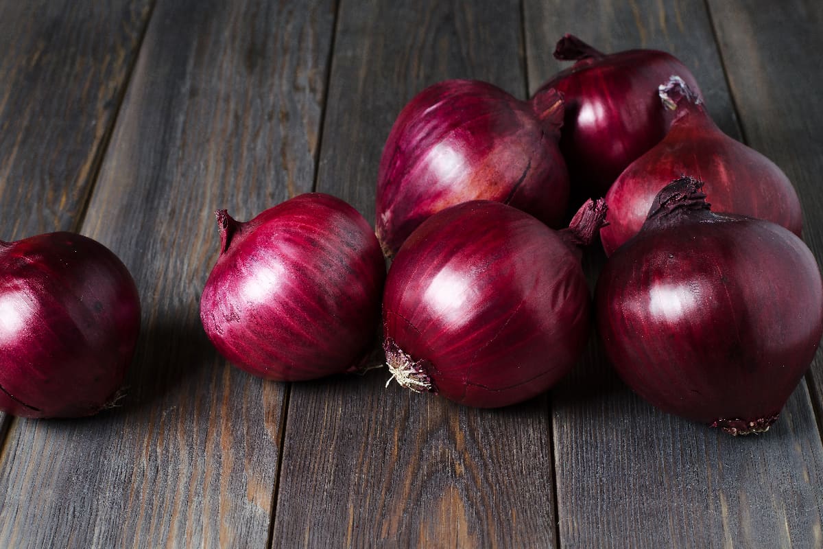 Lots of red onions on a brown wooden background