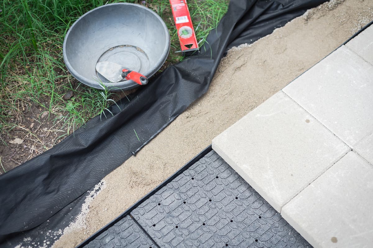 Weed barrier and leveling paver sand to hold the concrete patio stone on paver base panel with edging