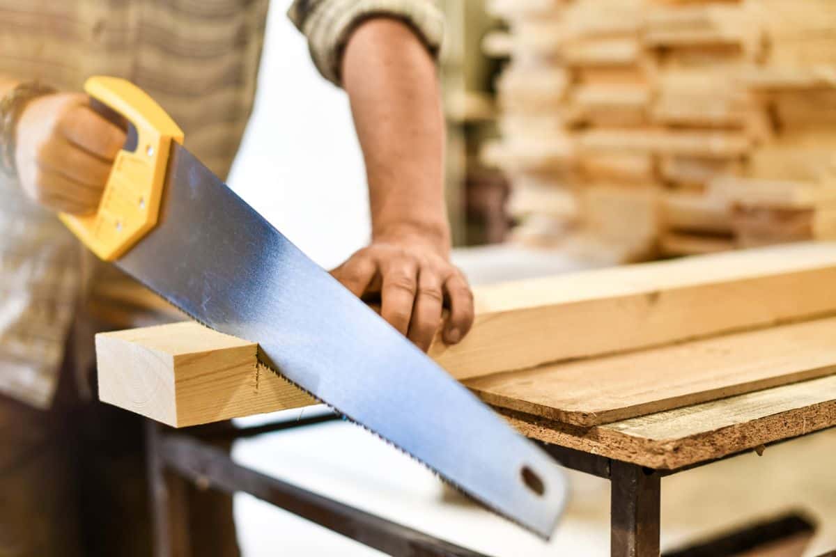Worker hands use a wood cutter or saw on wooden board. Carpenter work in action.