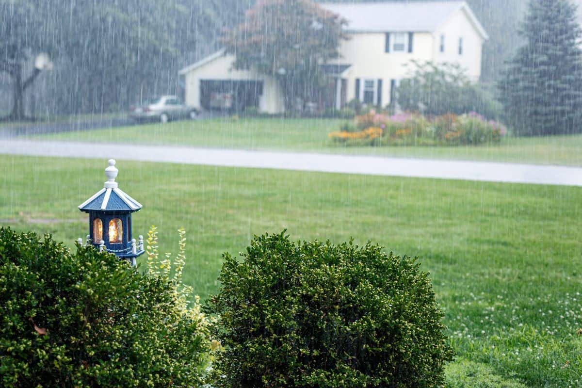A front yard wooden replica model lighthouse is illuminated during a drenching downpour