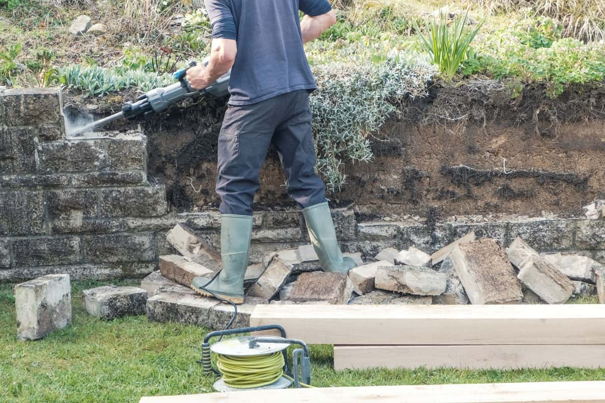 A man demolishing a garden stone wall to be replaced with oak sleepers, supporting a herbacious border