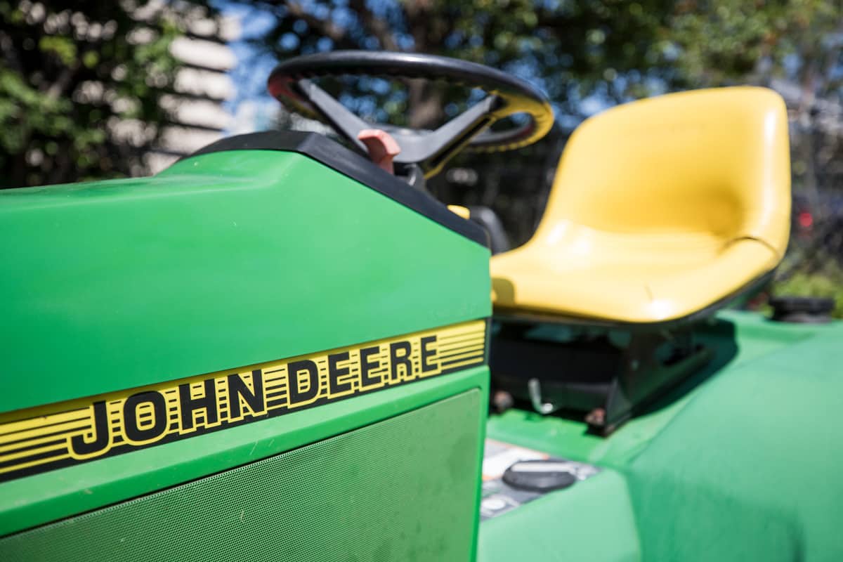 A motorcycle repair shop has a repaired John Deere lawn tractor outside of its facility on a sunny afternoon in the summertime.