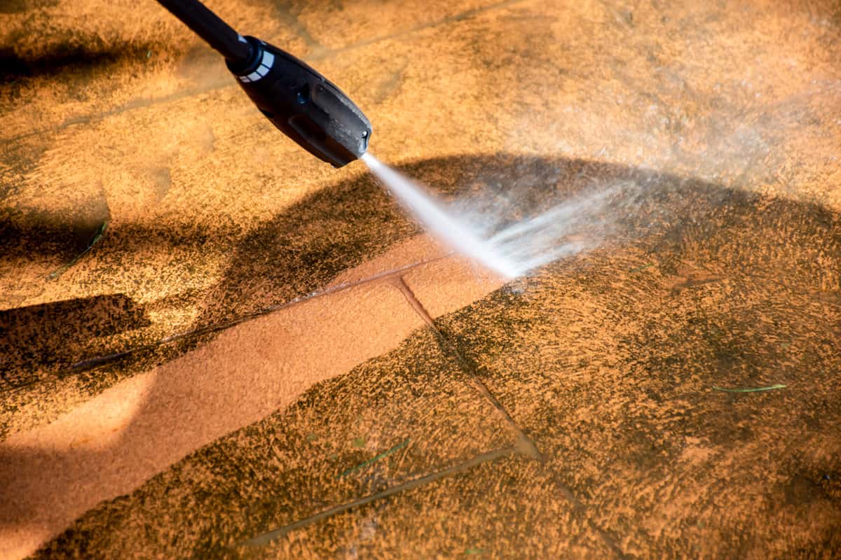 Cleaning backyard paving tiles pathway with high pressure washer. 