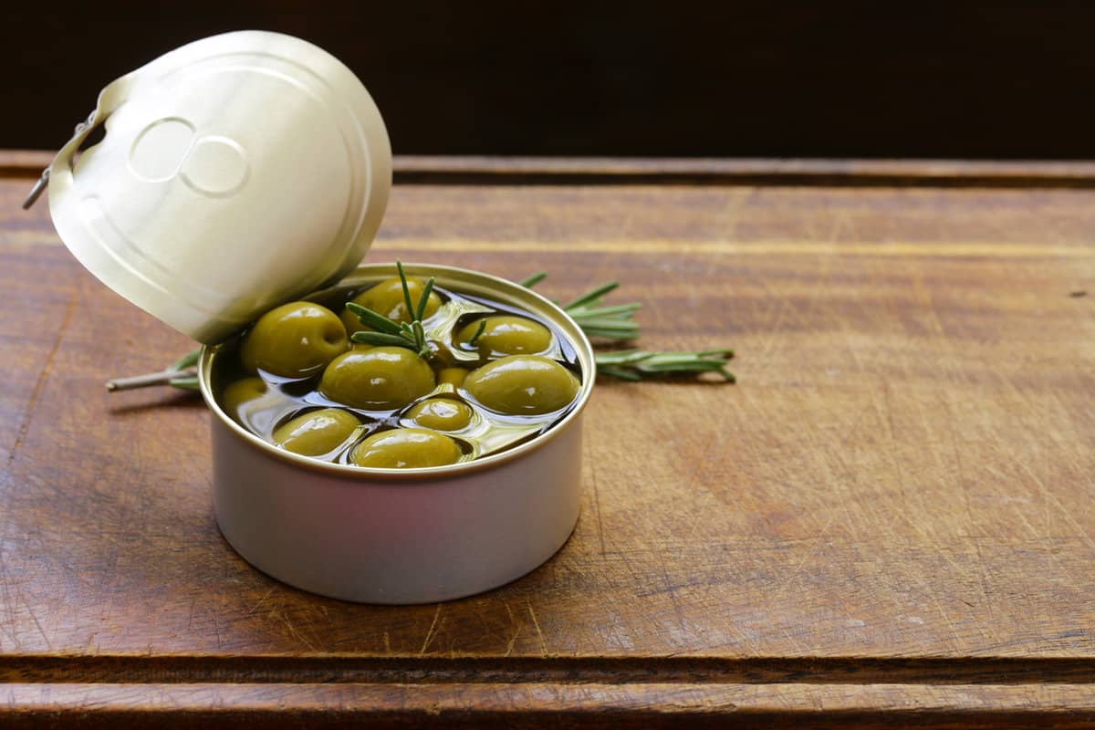 Organic canned green olives on a wooden table.