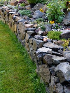 dry wall serves as a terrace terrace for the garden, where it holds a mass of soil. the wall is slightly curved, How To Push Back A Retaining Wall [Detailed Guide]