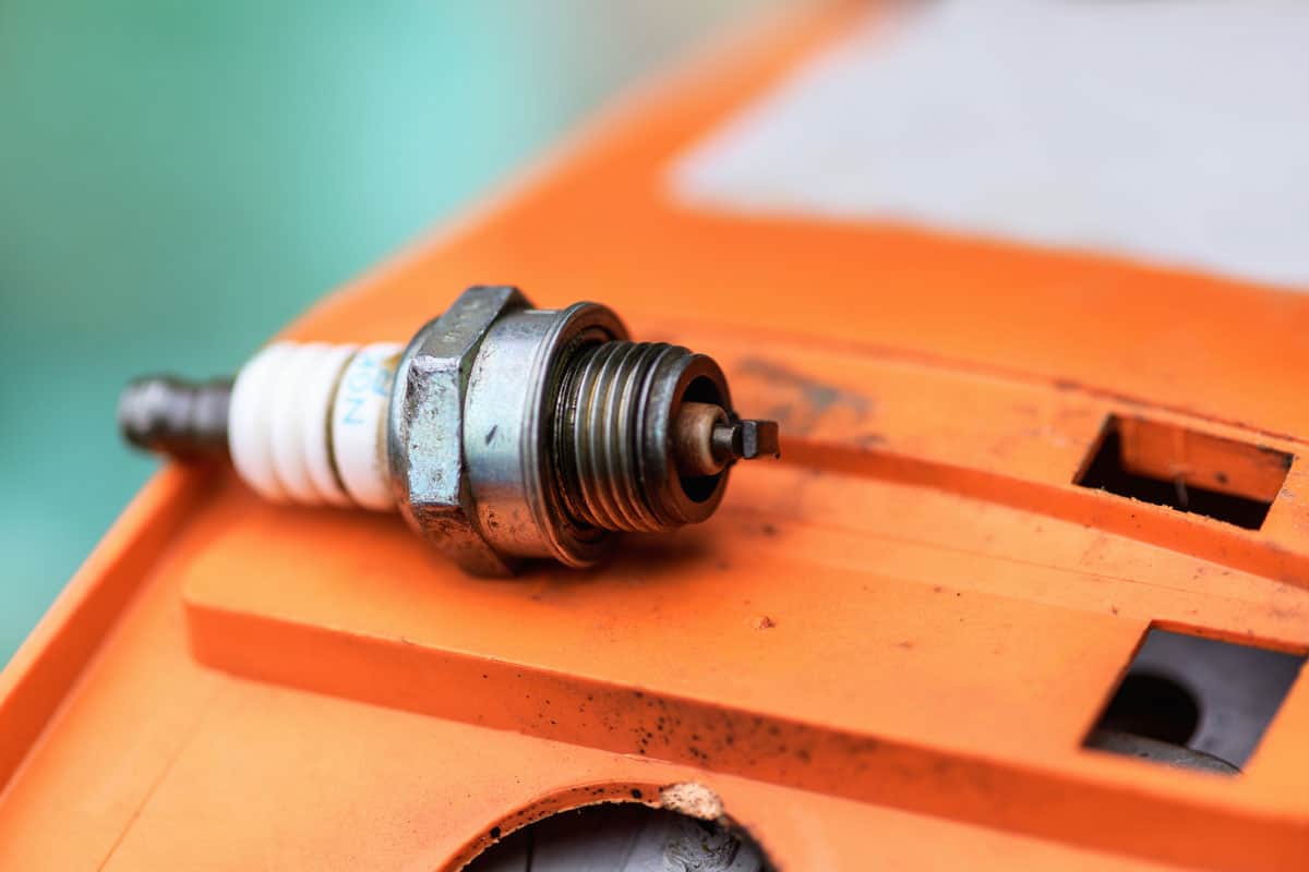 Non-working chainsaw spark plug lies on an orange surface