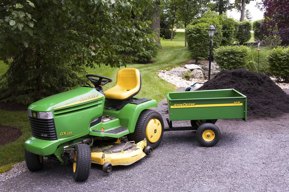 John Deere tractor with wagon in front of pile of garden mulch in a residential back yard
