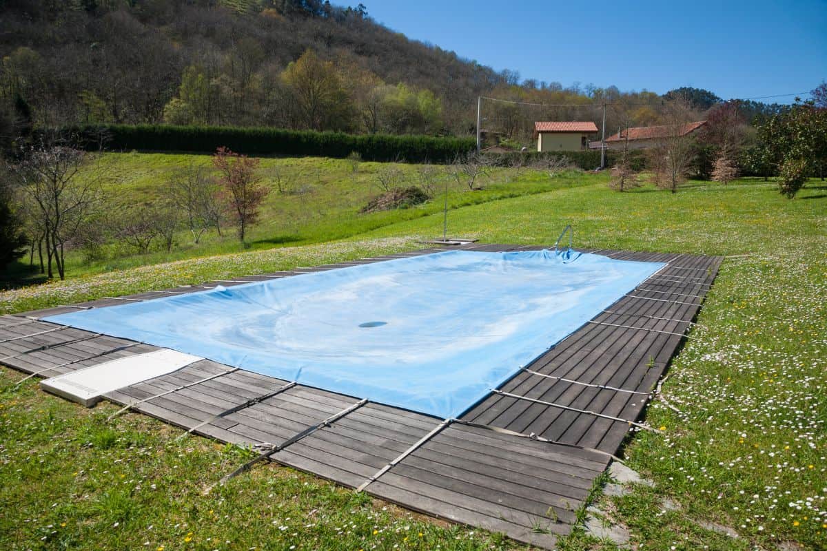 swimming pool with wooden curb closed and covered with blue tarp in Spring green meadow rounded by mountains in Nature in Asturias Spain Europe 