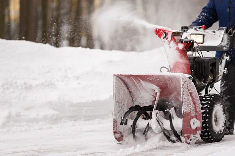 A man with a red snow-covered snow blower clears the area from snow. Clearing the area from snowfall, How To Start A Toro Snow Blower [In 5 Easy Steps]