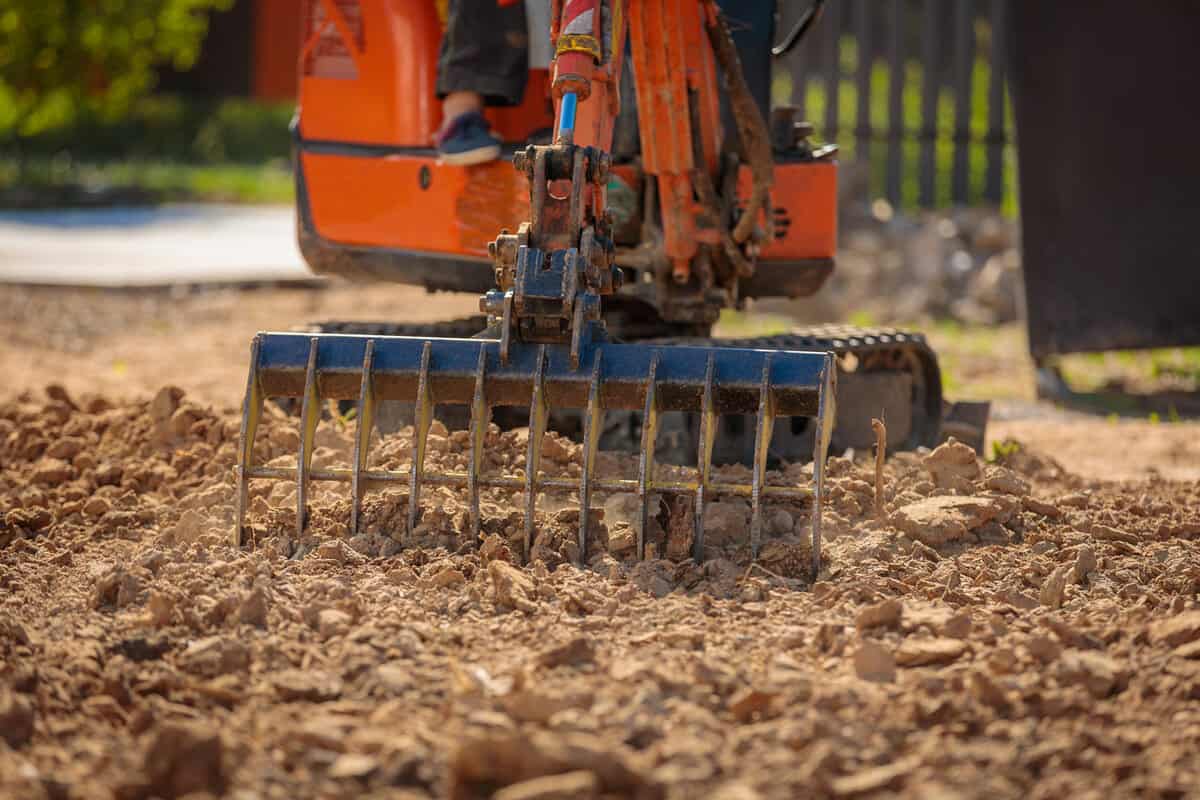 A mini excavator with a rake loosens the ground. landscape preparation