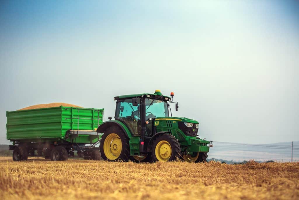 A modern John Deere 6115R tractor with the trailer on a yellow field.The 6115R has Premium ComfortView cab.