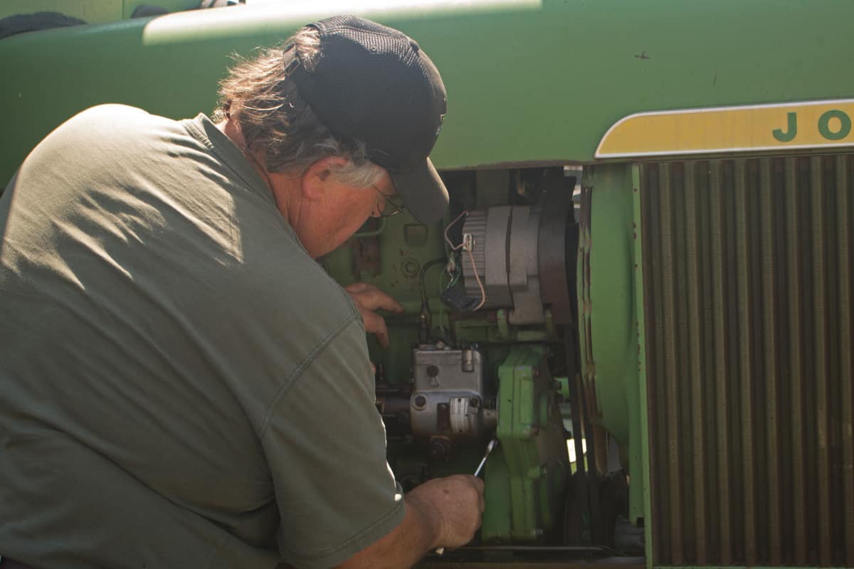 Agricultural Equipment Mechanic working on an antique John Deere tractor